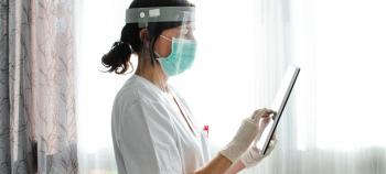 Nurse wearing PPE uses a secure messaging app on a tablet.